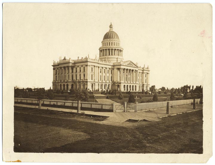 Capitol building with dome. surrounded by enclosed yard with small trees.