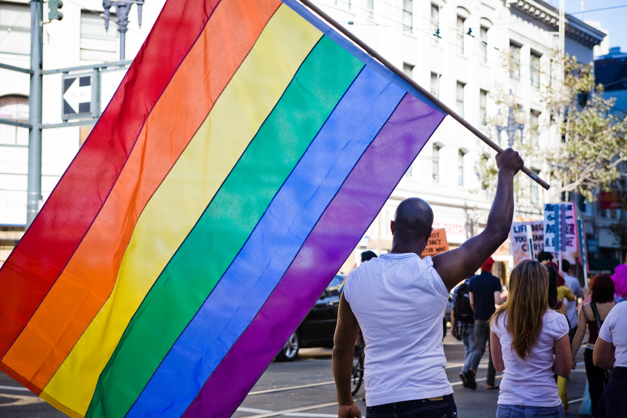 Protesters in street. Man carries large rainbow flag.