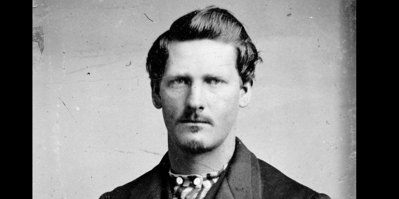 Photo portrait of Wyatt Earp as a young man with small mustache and slight beard. Serious look on his face.