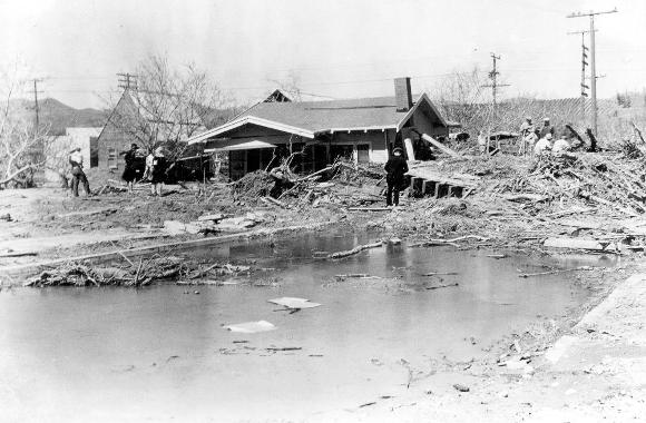 Shows flood wreckage in Santa Paula, California. March 18, 1928. Including a house destroyed by the flood and several people attempting to clean up.