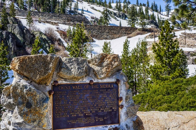 A sign in front of a snowy mountain with trees.