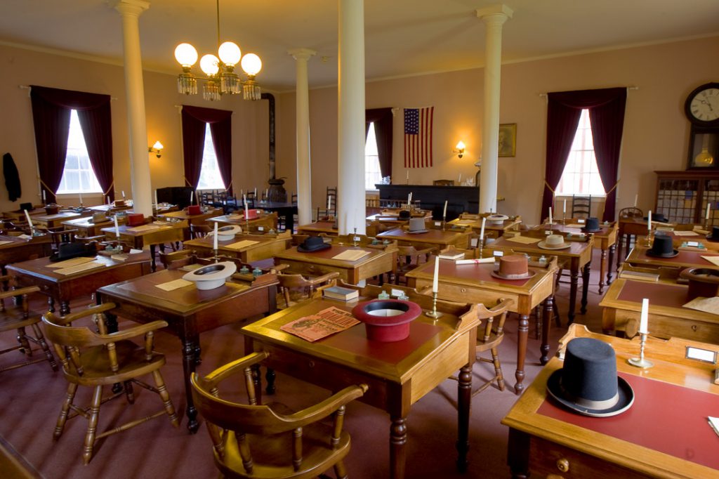 Inside Benicia Capitol building room has wooden desks to replicate what it looked like in 1850s. Each desk has a candle in holder.