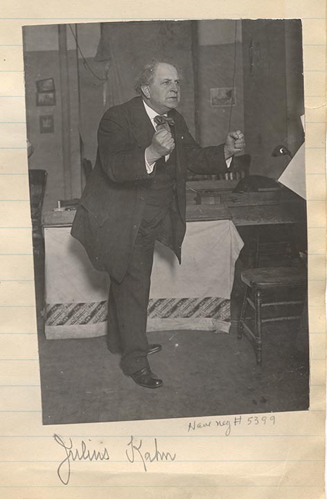 Full-length portrait of Julius Kahn standing in a room clenching both of his fists, arms extended in front of him. Text written under photo: "Julius Kahn."