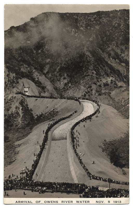 View of the arrival of Owens River water at the San Fernando Reservoir on November 5, 1913. The water is seen cascading down the aqueduct with a large crowd looking on.