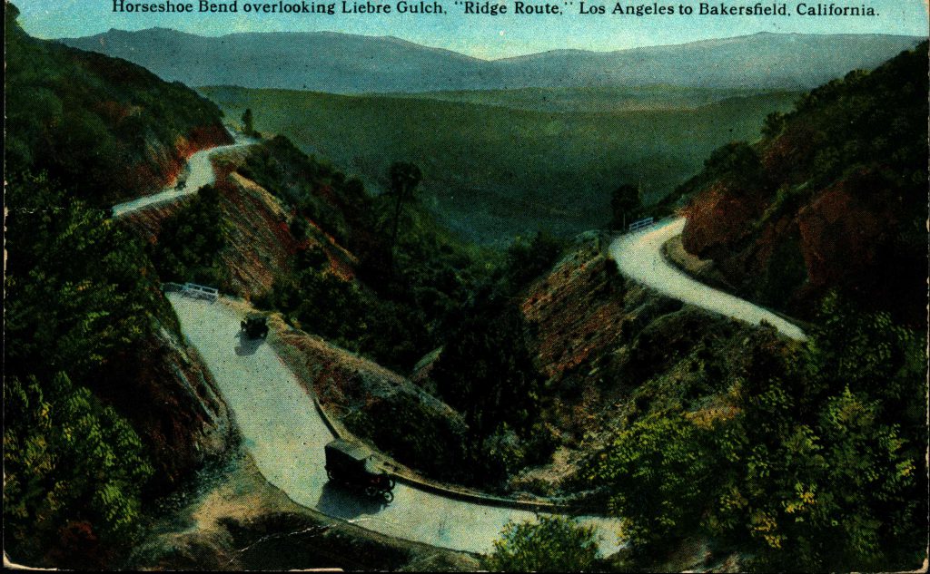 Cars drive along winding mountain road next to gulch.