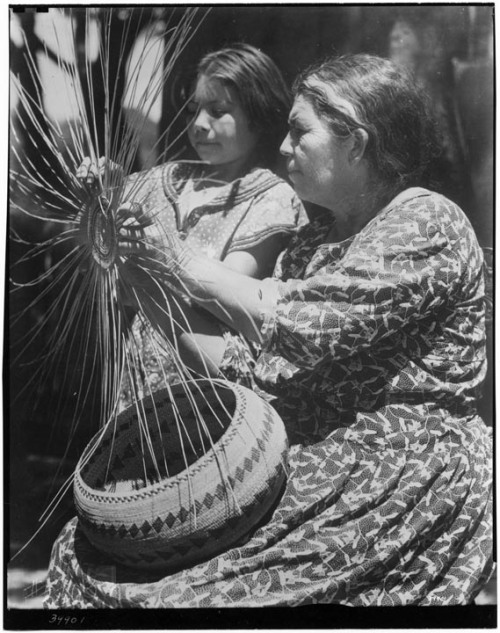 Annie Burke showing girl how to weave reeds for a basket