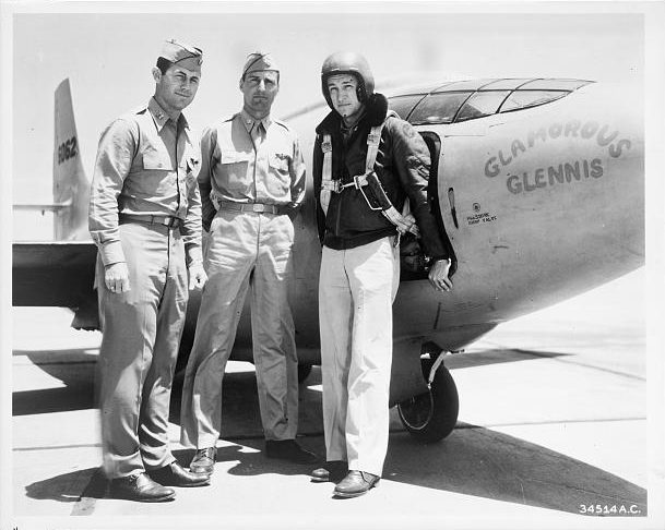 Photograph shows "Chuck" Yeager, Gus Lundquist, and Jim Fitzgerald wearing a flight suit, standing next to the Bell XS-1 rocket research airplane "Glamorous Glennis."