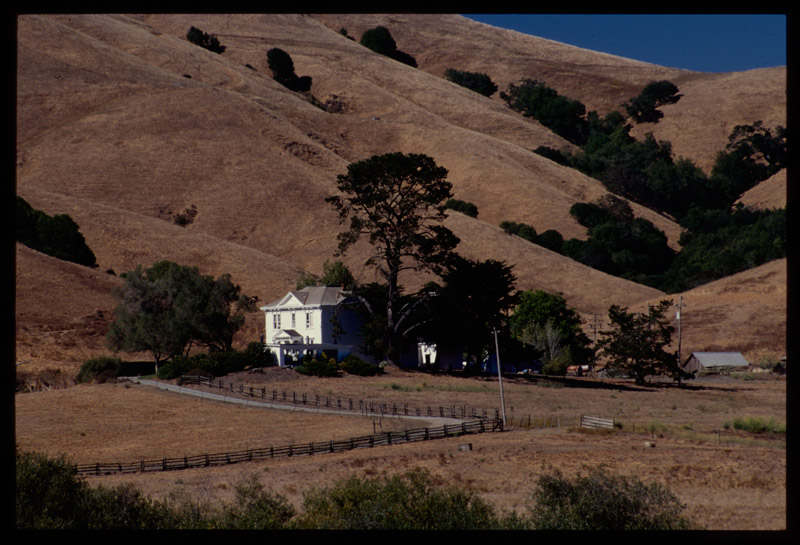 Shows a white house against a backdrop of golden hills