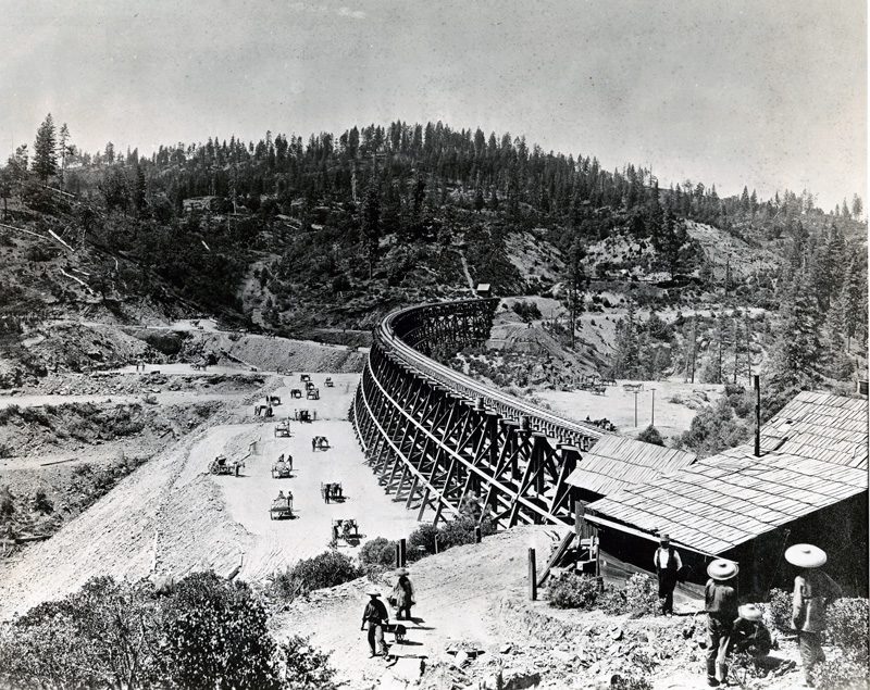 Shows several workers, some of them Chinese, working on building a railroad trestle