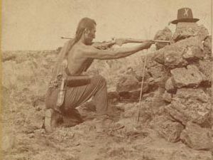 A posed shot taken by Muybridge showing a Modoc man taking aim with a gun