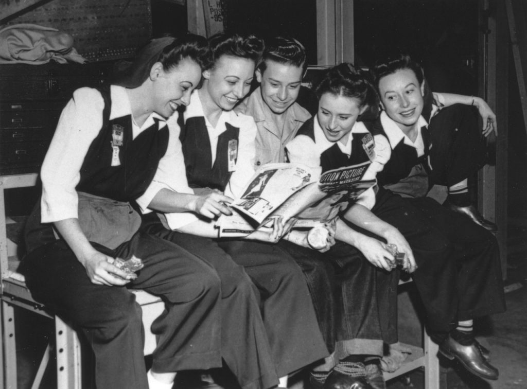 Group of young women smiling as they look at movie magazine.