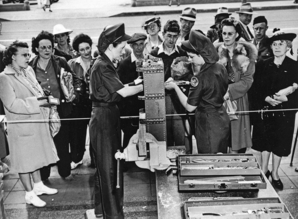 Two women demonstrating how to use tools to a group of mostly women.