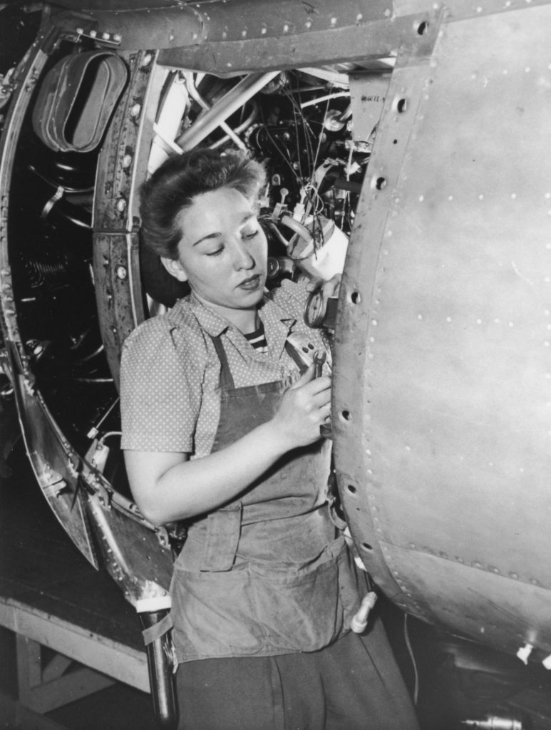 Woman with gauge and wrench working on aircraft during production drive, c. 1941-45.