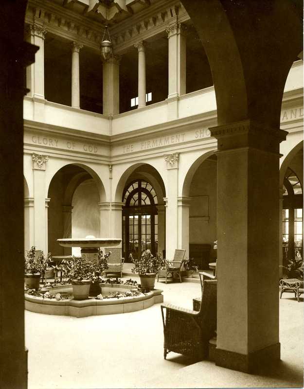 A black and white photograph of a courtyard with a fountain in the middle.,